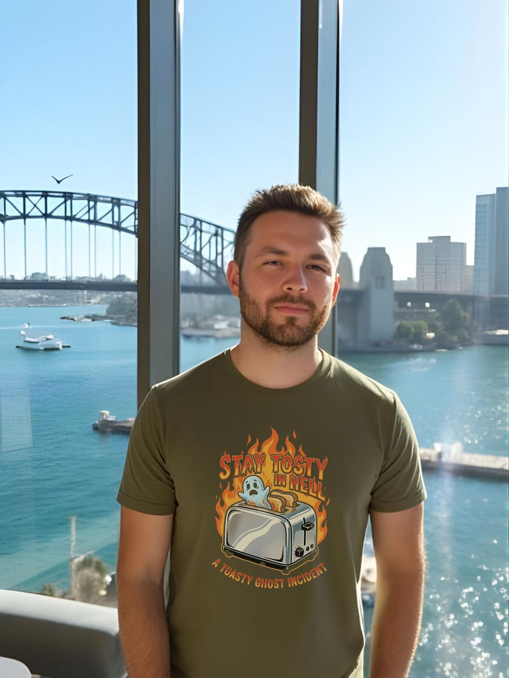 Man wearing a green t-shirt with a graphic design, standing in front of a large window with a cityscape view.