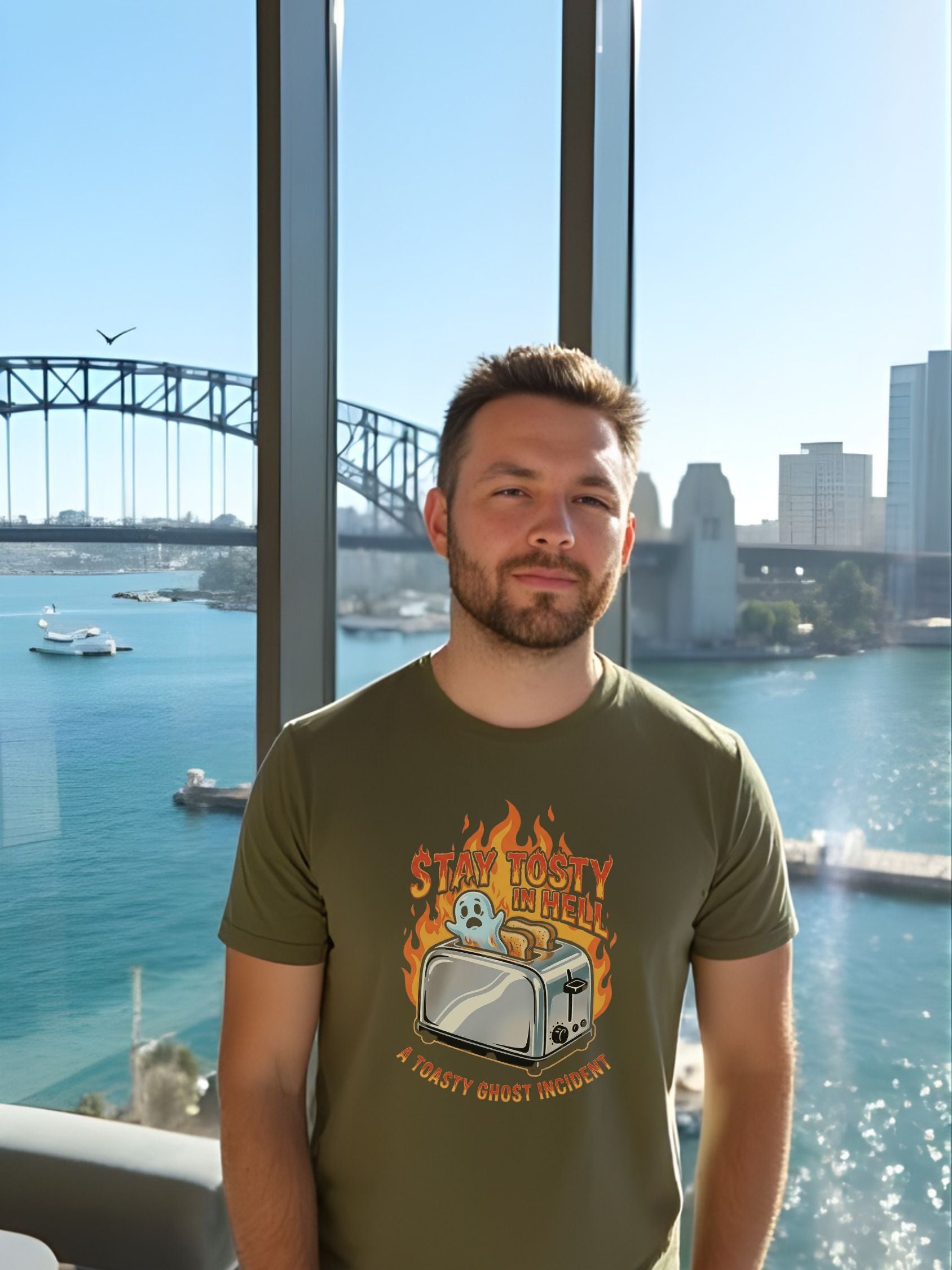 Man wearing a green t-shirt with a graphic design, standing in front of a large window with a cityscape view.