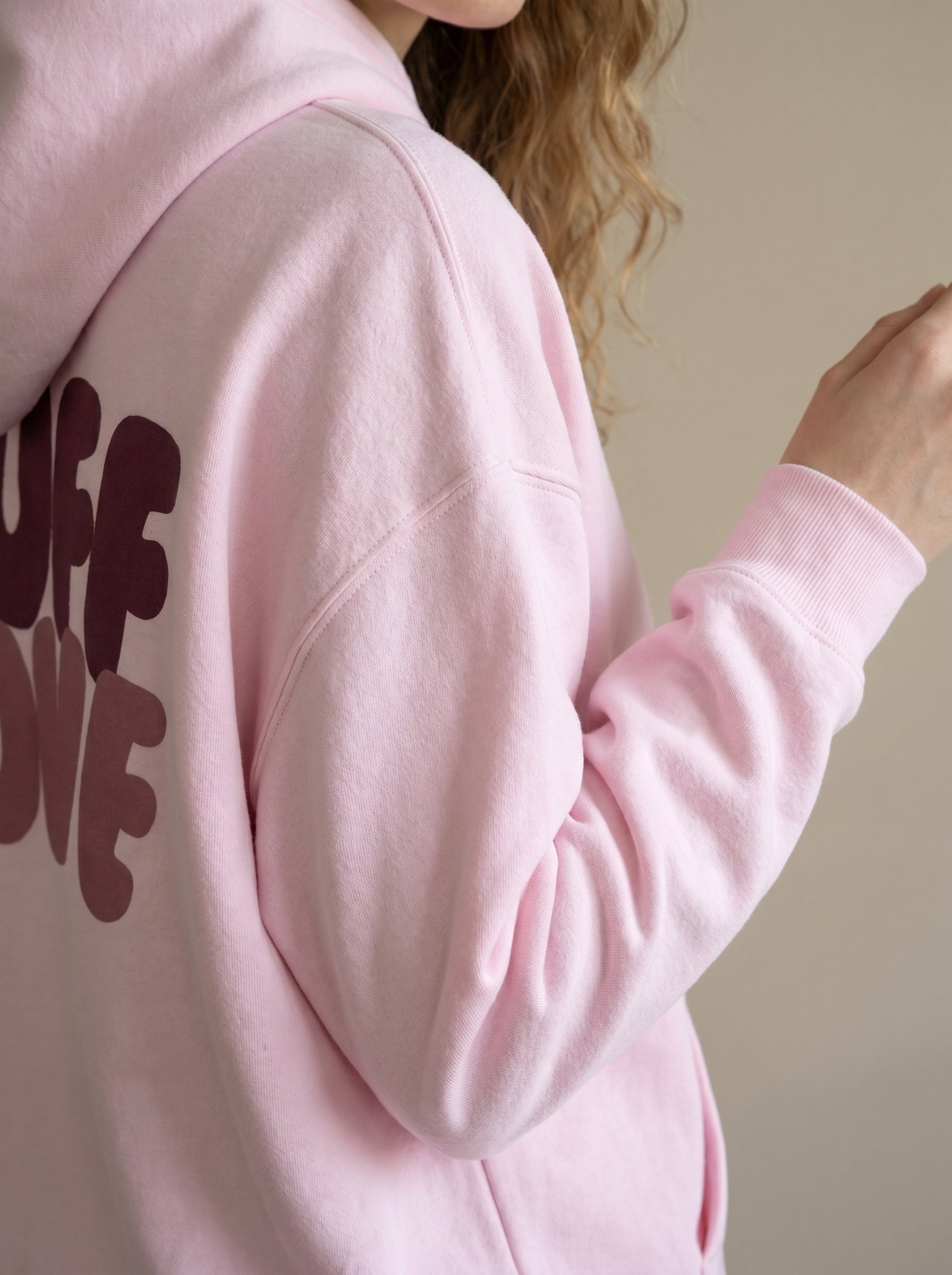 Close-up of a pink hoodie with text on the back against a neutral background