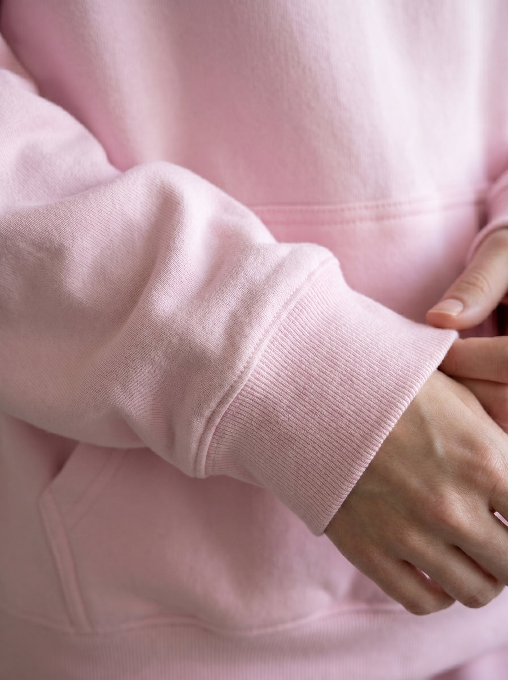 Close-up of a person wearing a pink hoodie with a focus on the sleeve and hand.