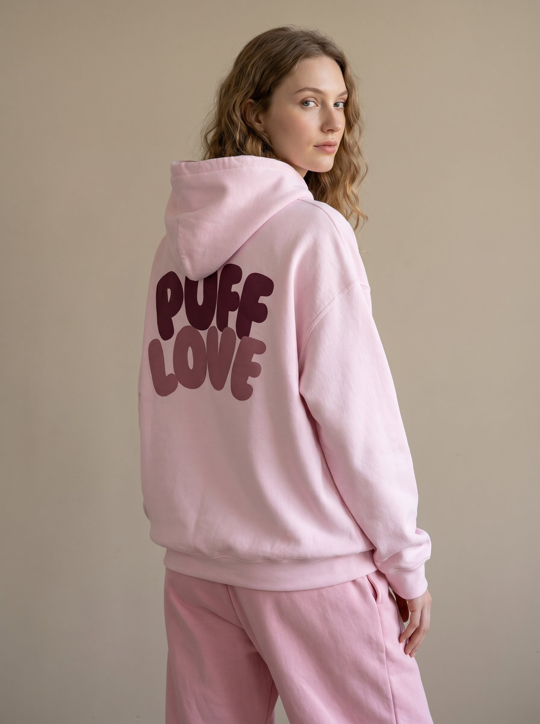 Person wearing a pink hoodie with 'Puff Love' text on the back against a beige background