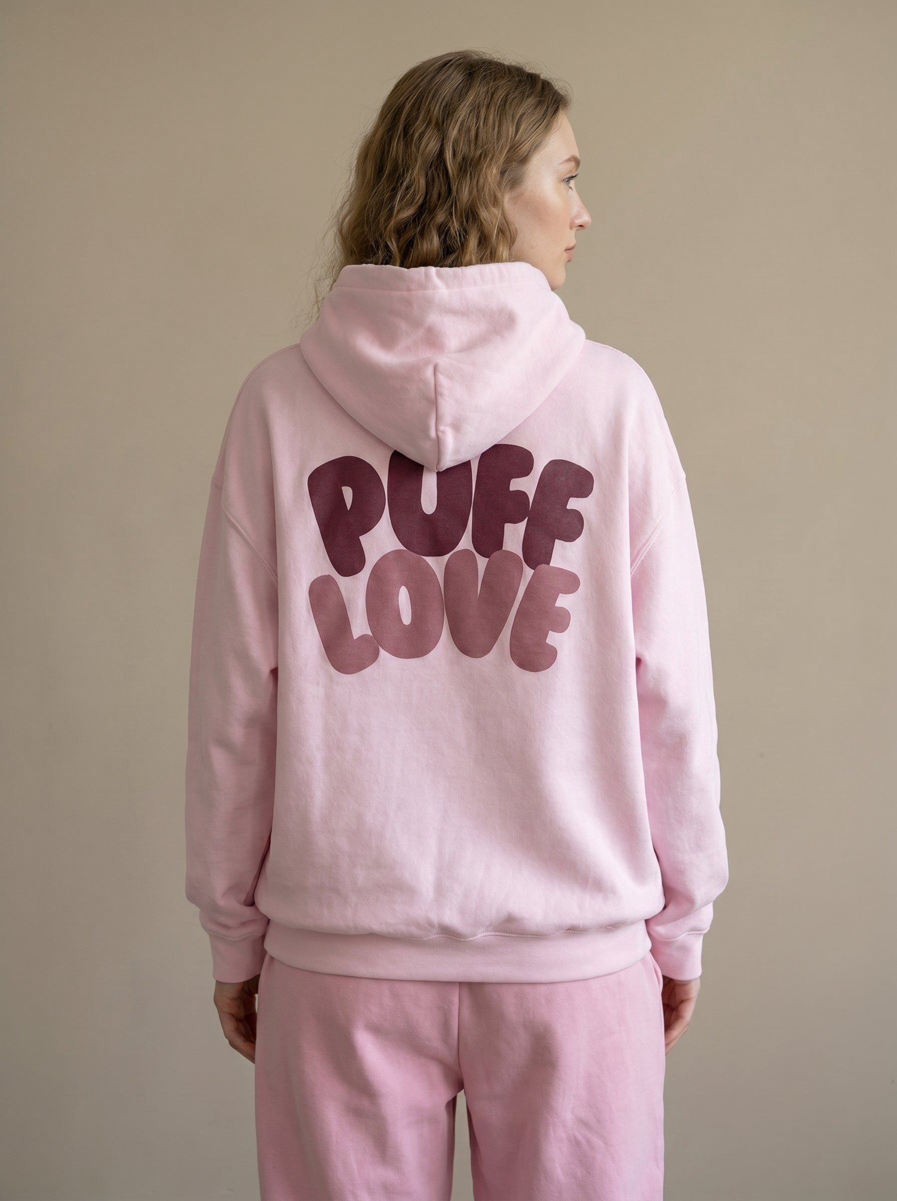 Person wearing a pink hoodie with 'PUFF LOVE' text on the back against a beige background