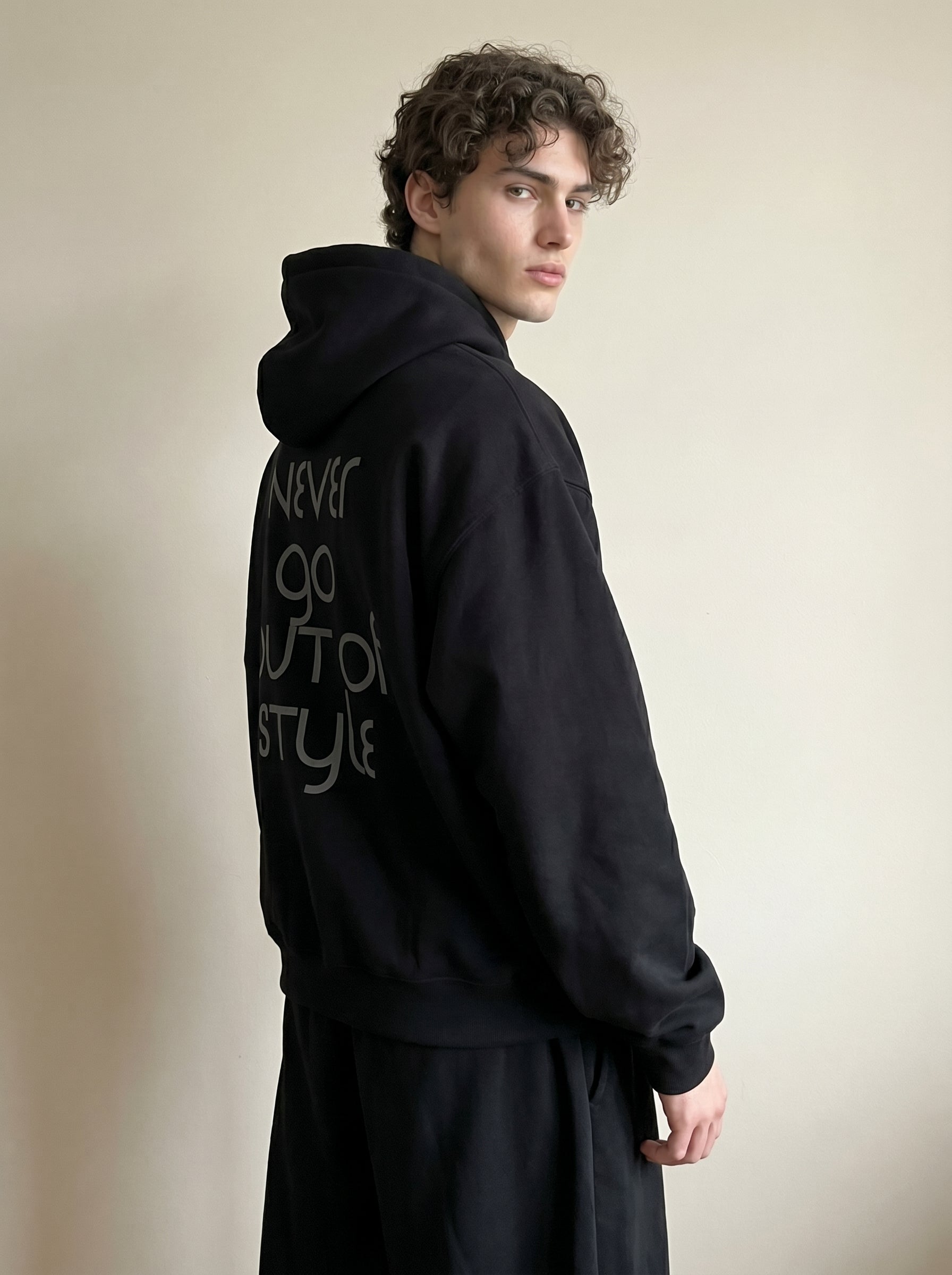 Person wearing a black hoodie with text on the back against a plain background