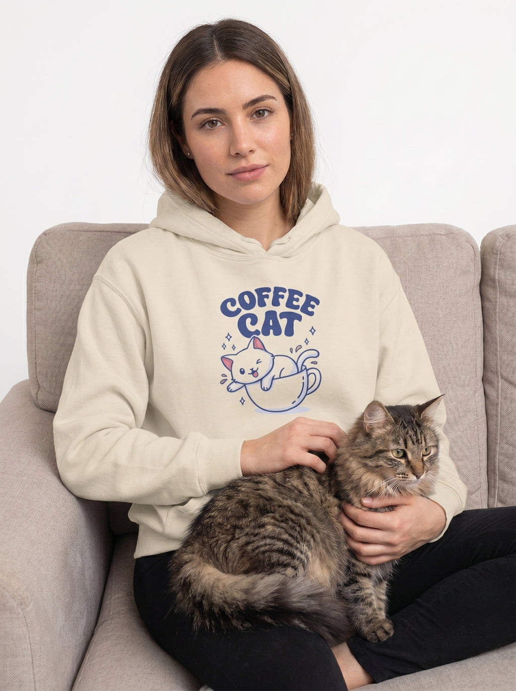 Woman wearing a hoodie with 'Coffee Cat' design, sitting on a couch with a cat.