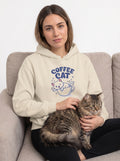 Woman wearing a hoodie with 'Coffee Cat' design, sitting on a couch with a cat.