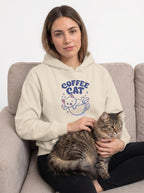 Woman wearing a hoodie with 'Coffee Cat' design, sitting on a couch with a cat.