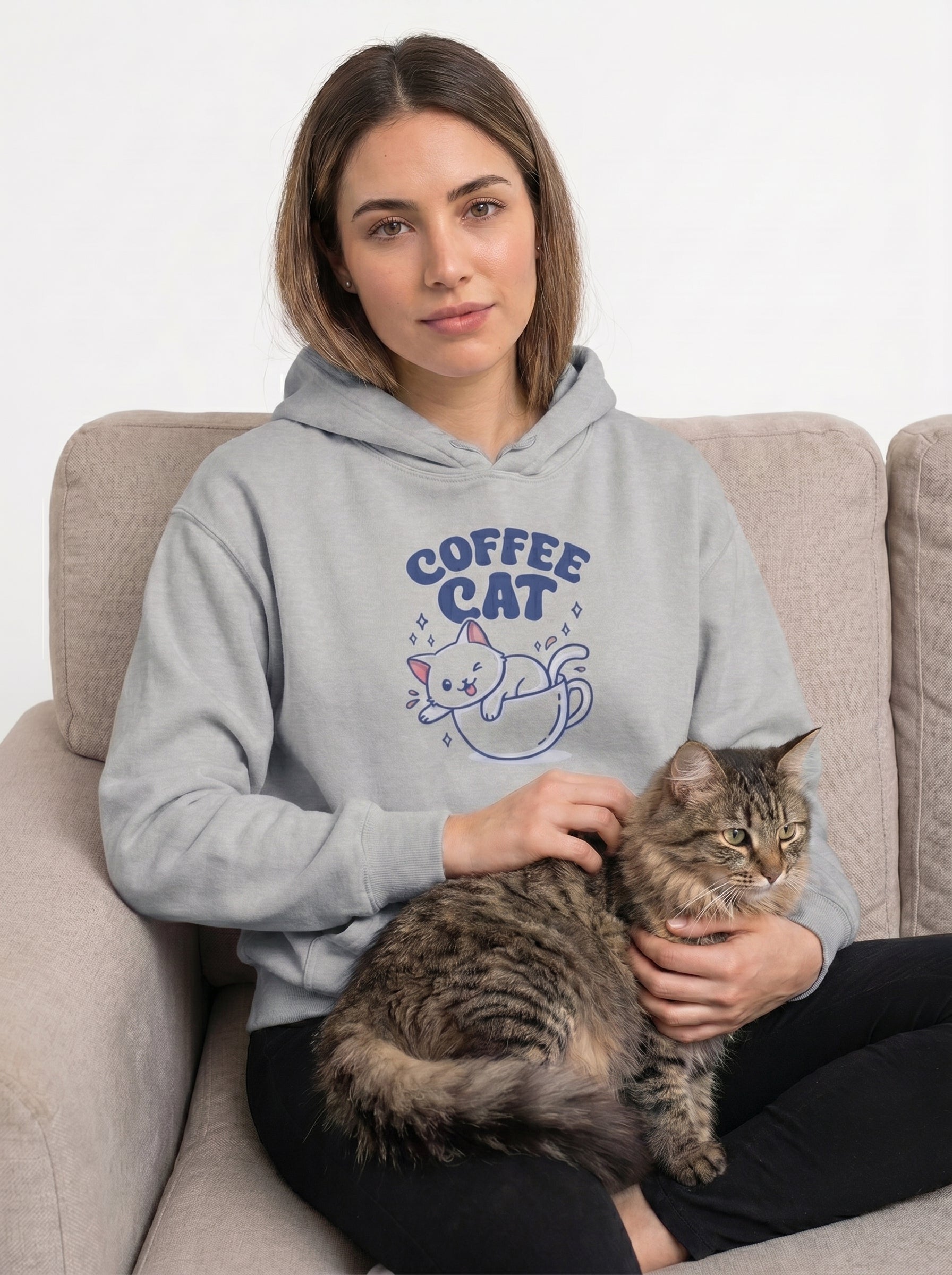 Woman wearing a gray hoodie with 'Coffee Cat' design, sitting on a couch with a cat.