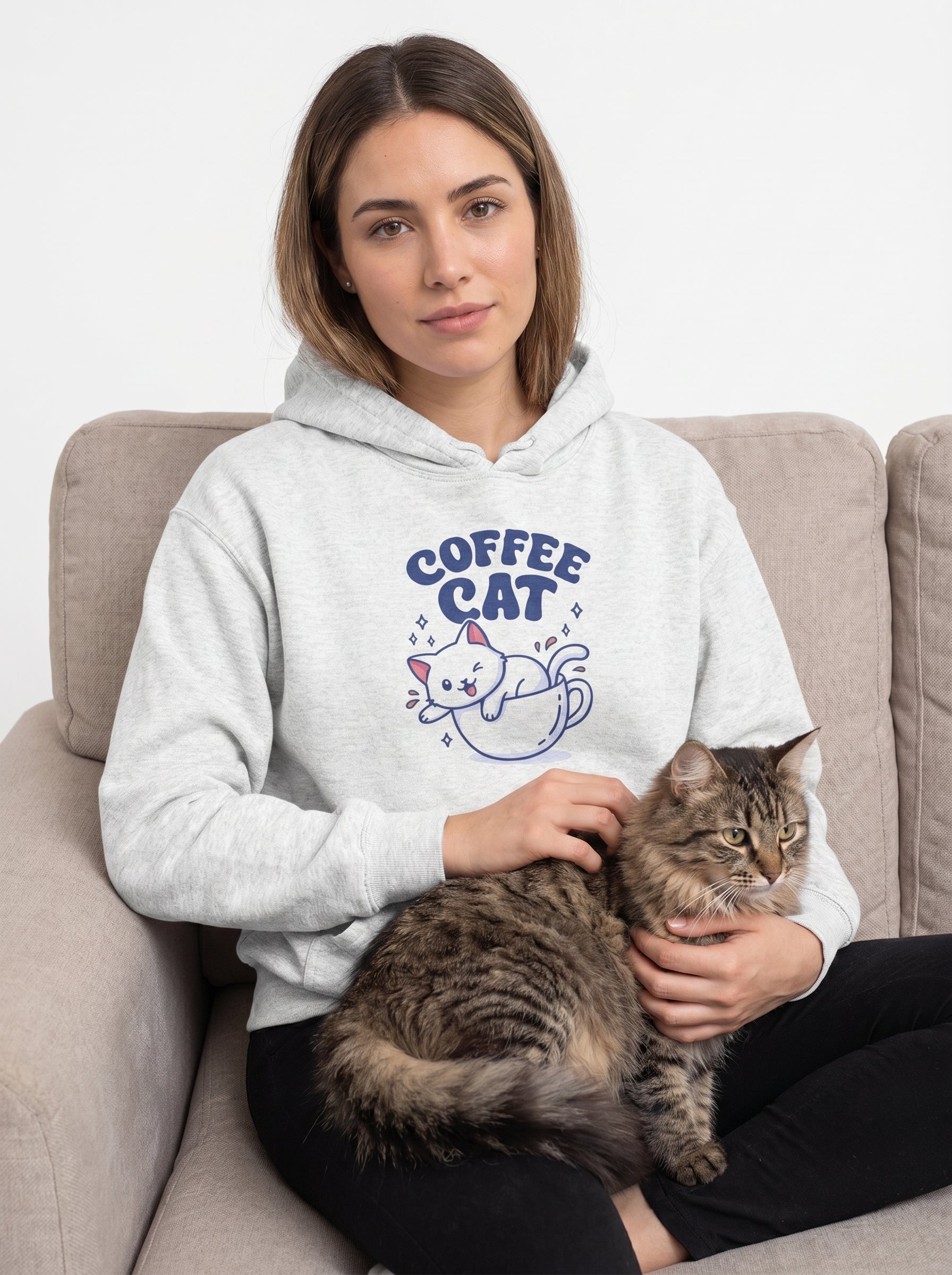 Woman wearing a 'Coffee Cat' hoodie holding a cat on a couch.