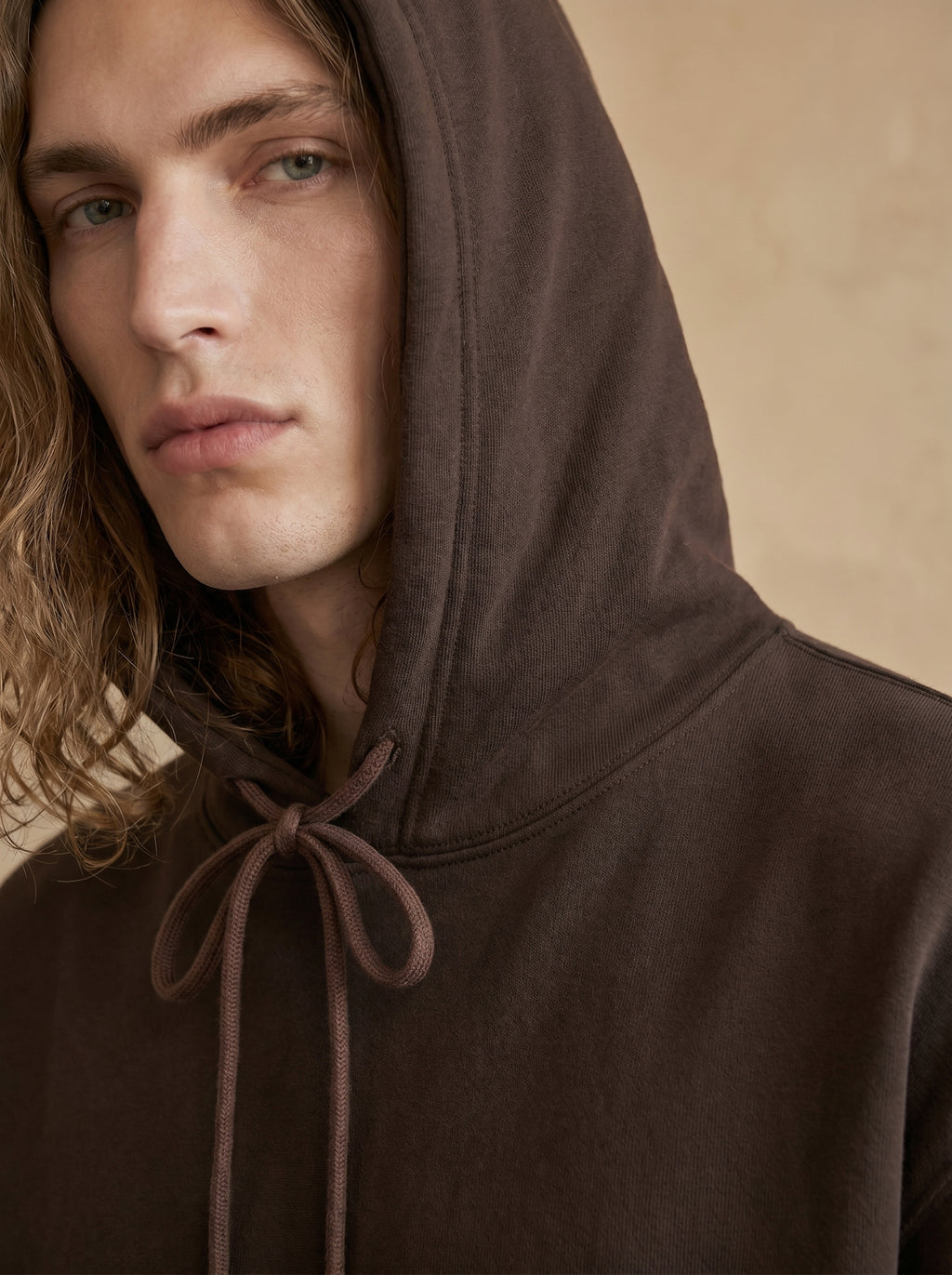 Person wearing a brown hooded garment against a beige background
