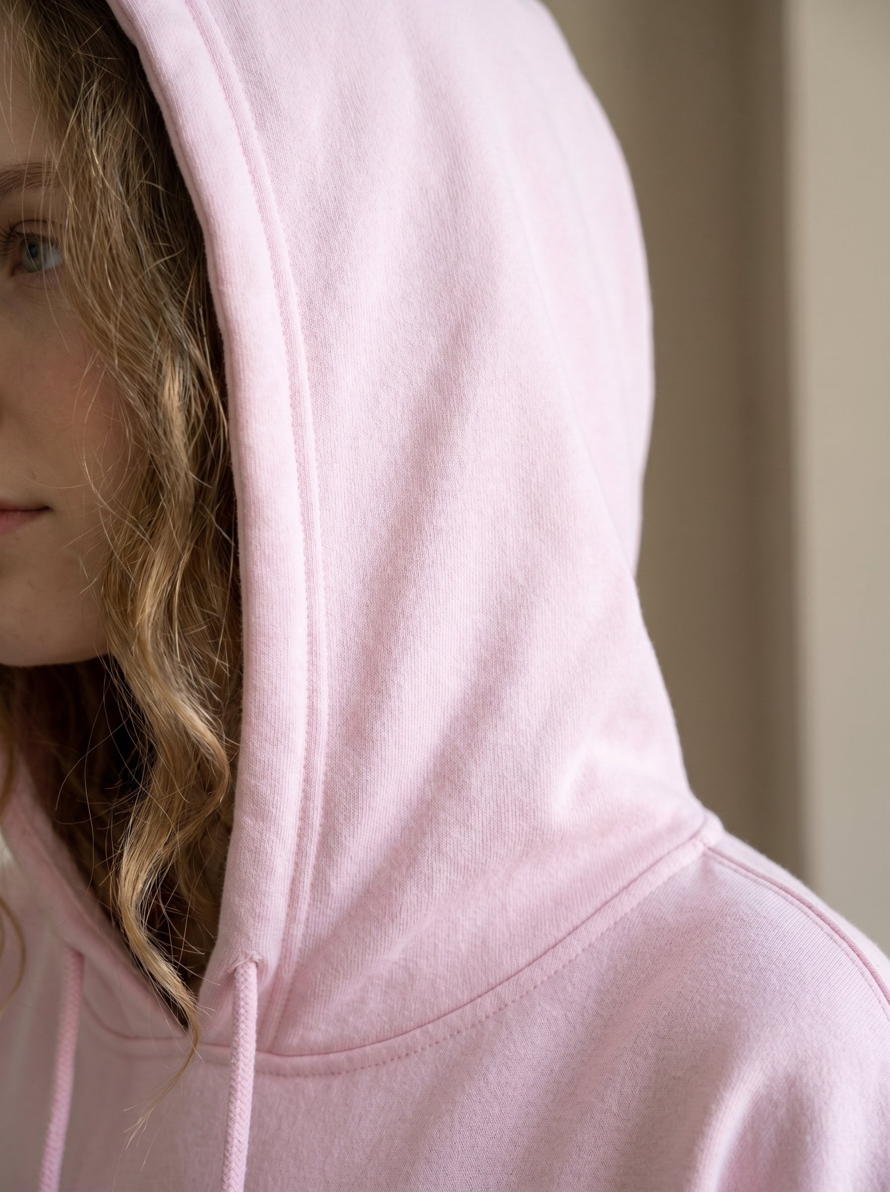 Person wearing a light pink hoodie with a neutral background