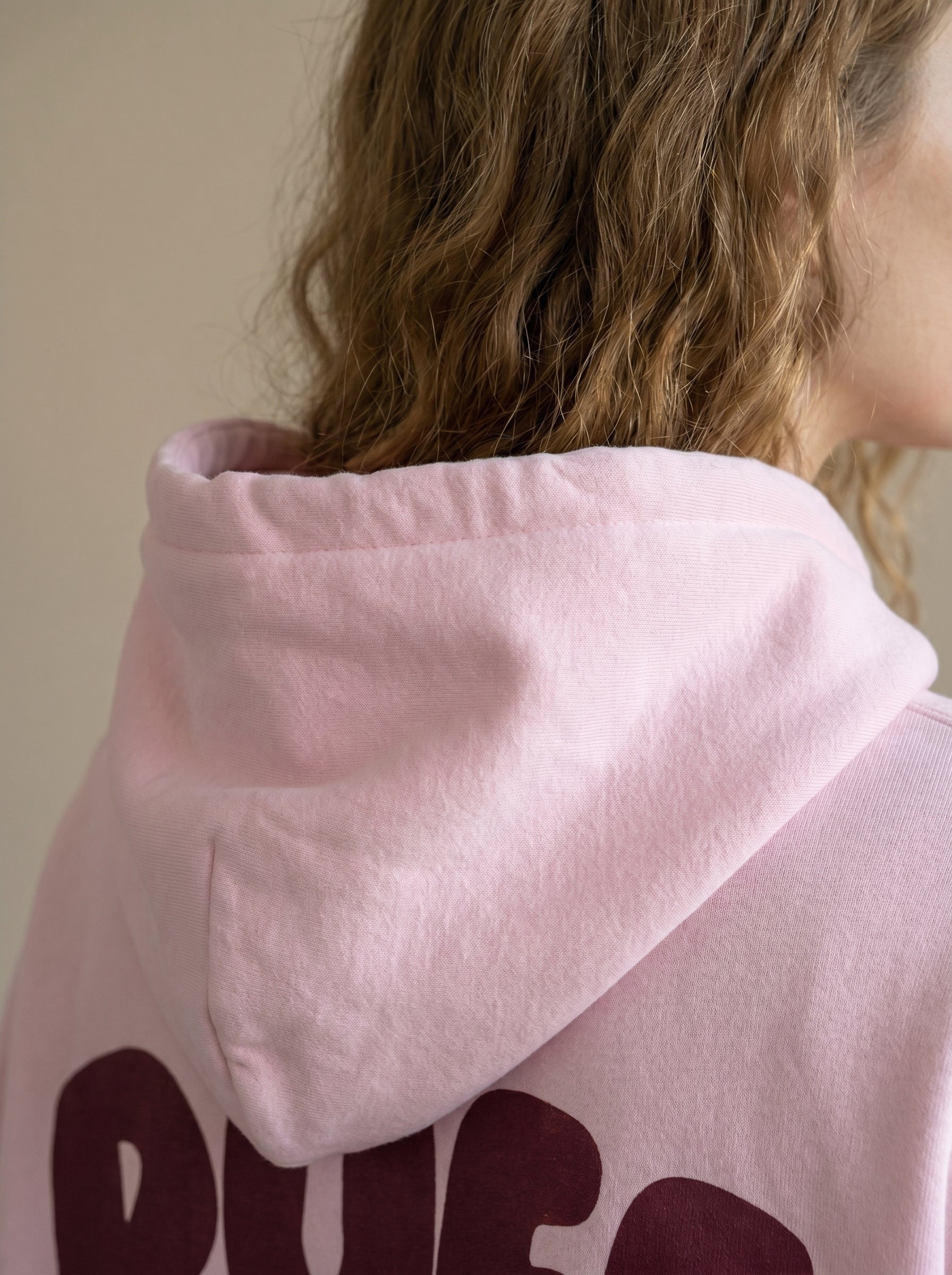 Pink hoodie with text worn by a person, blurred background