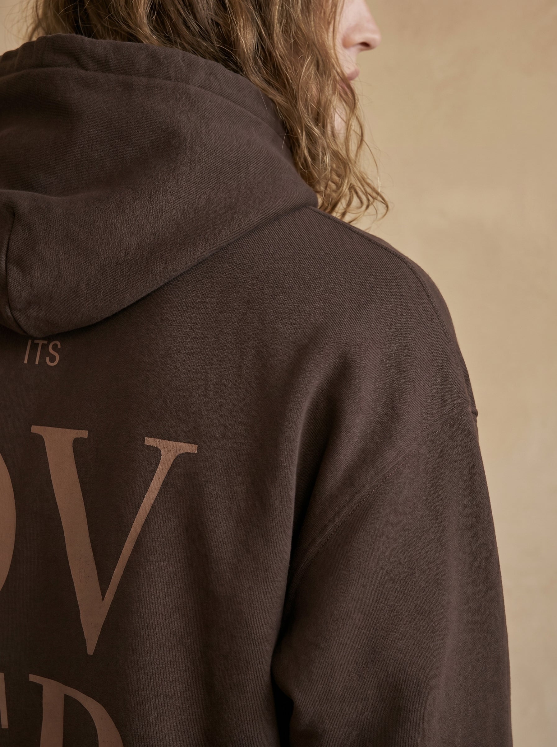 Brown hoodie with text on the back against a beige background