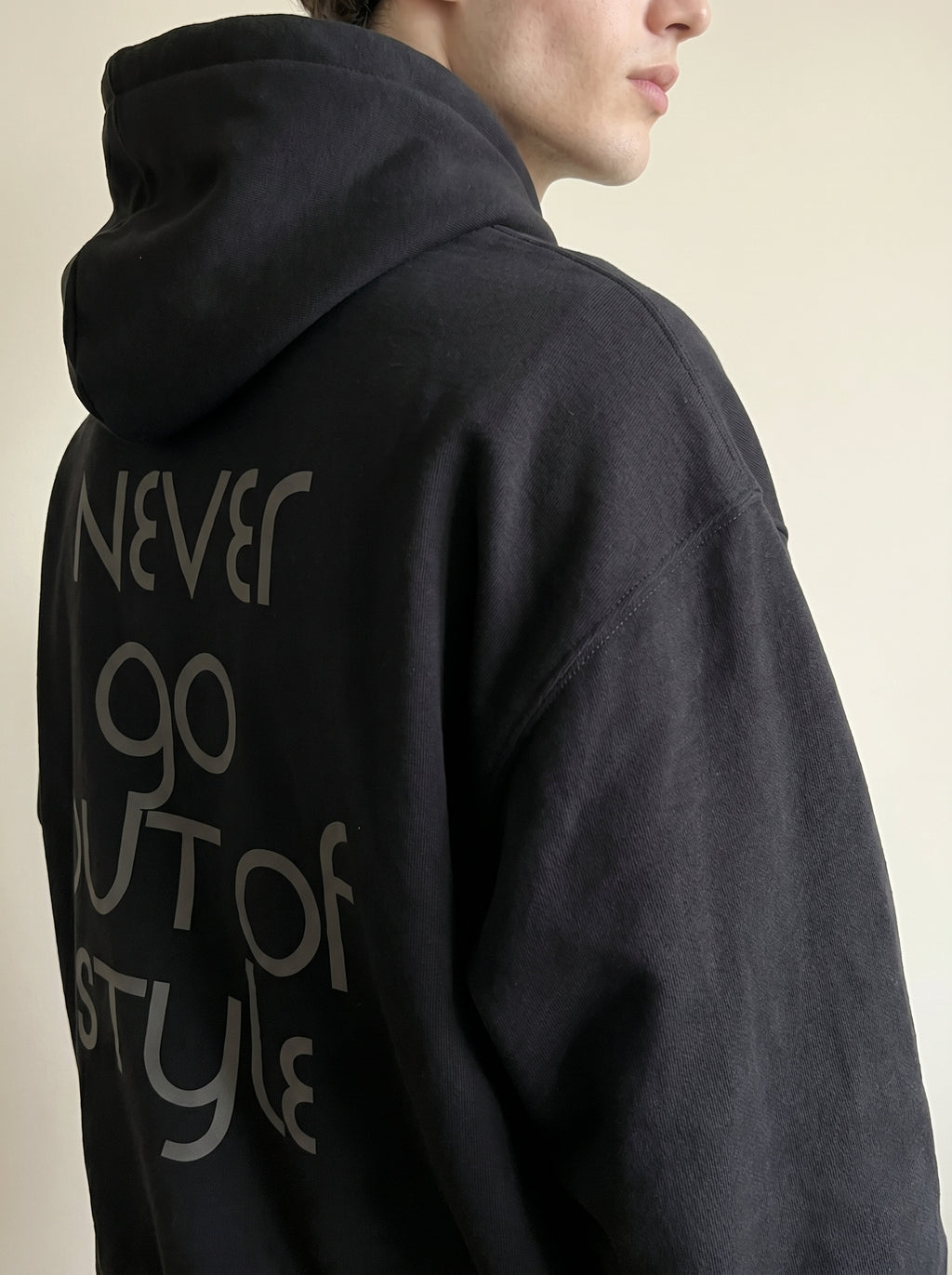 Person wearing a black hoodie with text on the back against a beige background