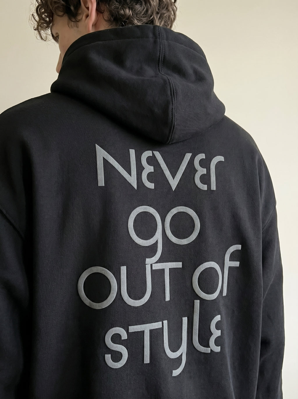 Person wearing a black hoodie with 'Never go out of style' text on the back.
