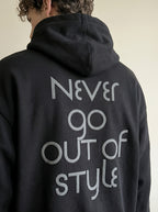 Person wearing a black hoodie with 'Never go out of style' text on the back.
