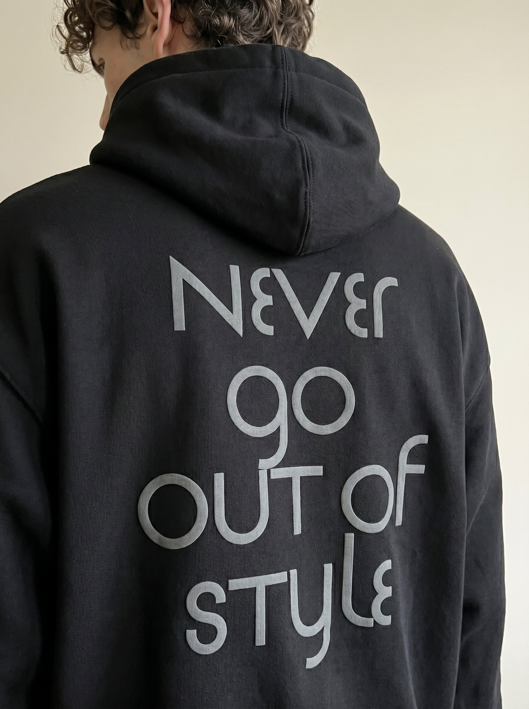 Person wearing a black hoodie with 'Never go out of style' text on the back.